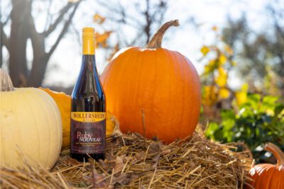 A bottle of Wollersheim's Ruby Nouveau glowing in the warm sunshine, sitting atop a bale of golden hay, surrounded by bright orange pumpkins.