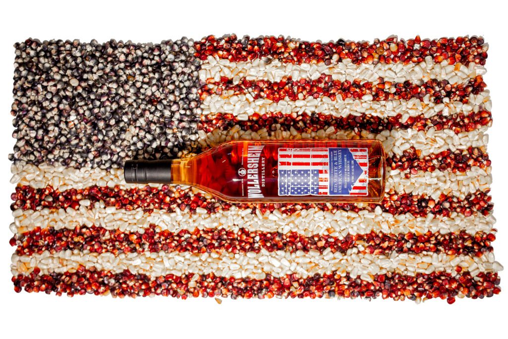 A bottle of Red White & Blue Whiskey sitting atop a US flag made of corn.